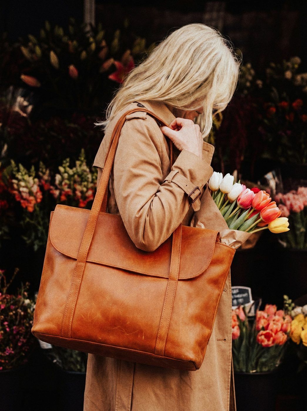 Femme portant un cabas en cuir cognac devant un étal de fleurs